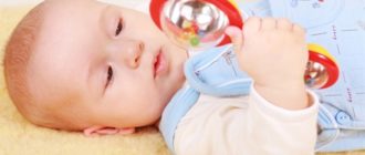 грудничок лежит в кроватке и разглядывает погремушку